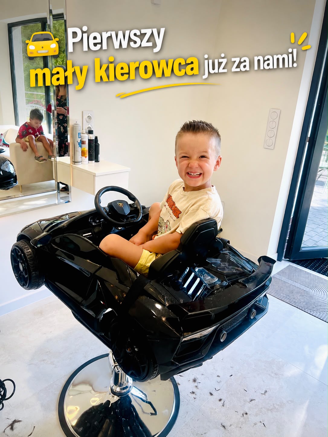 Uśmiechnięty chłopiec po strzyżeniu w fotelu w kształcie samochodu.